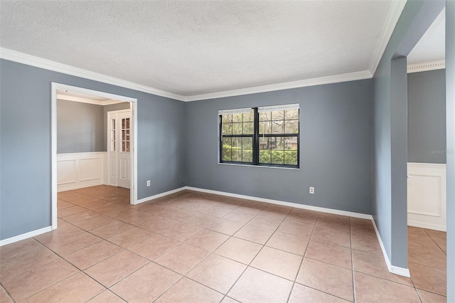 empty room with a textured ceiling, light tile patterned flooring, wainscoting, and ornamental molding