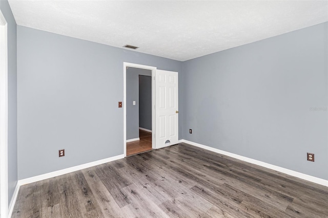 empty room with visible vents, a textured ceiling, baseboards, and wood finished floors