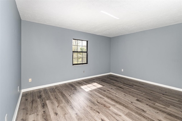 spare room with a textured ceiling, baseboards, and wood finished floors