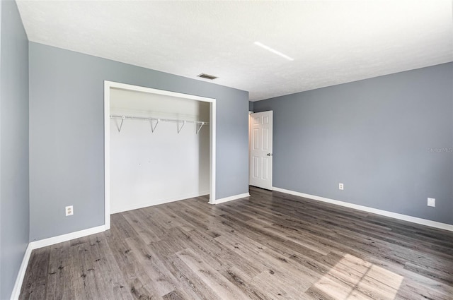 unfurnished bedroom featuring a closet, visible vents, baseboards, and wood finished floors