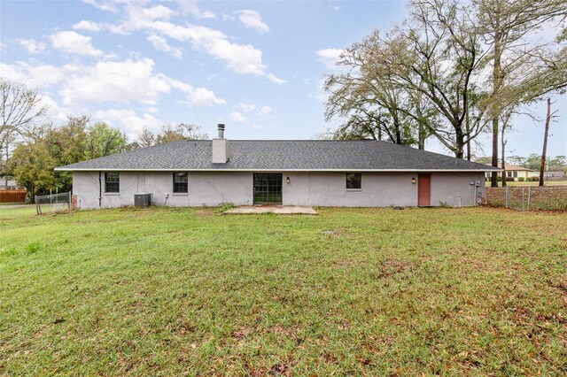 rear view of house featuring stucco siding, a lawn, central AC, fence, and a chimney