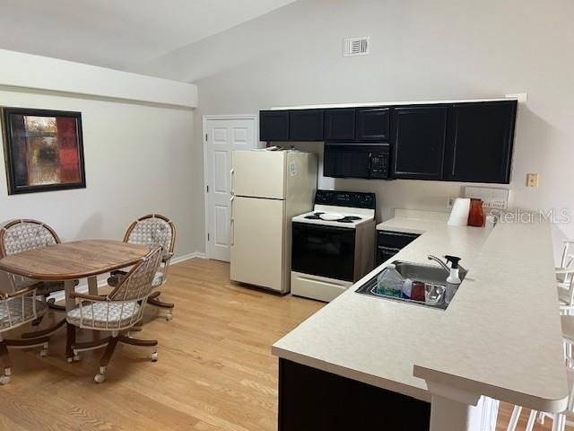 kitchen with light wood-type flooring, white appliances, vaulted ceiling, and sink