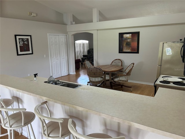 kitchen featuring vaulted ceiling, hardwood / wood-style floors, electric range, stainless steel refrigerator, and sink