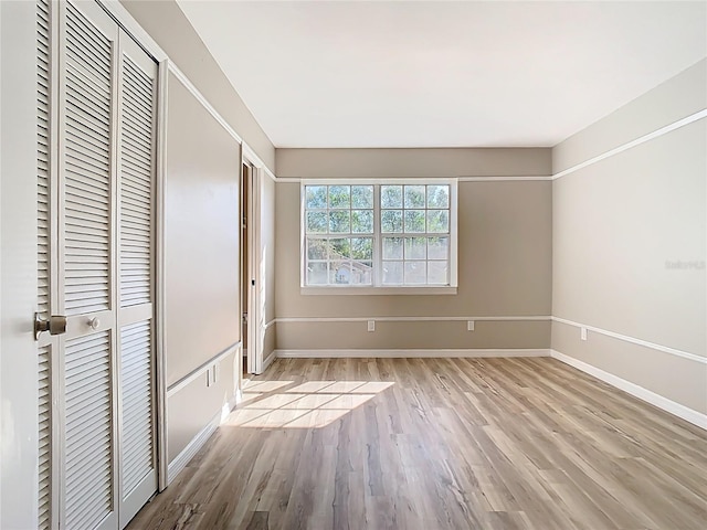 unfurnished bedroom with wood finished floors, baseboards, and two closets