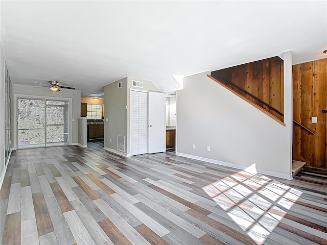 unfurnished living room with visible vents, a ceiling fan, wood finished floors, stairway, and baseboards