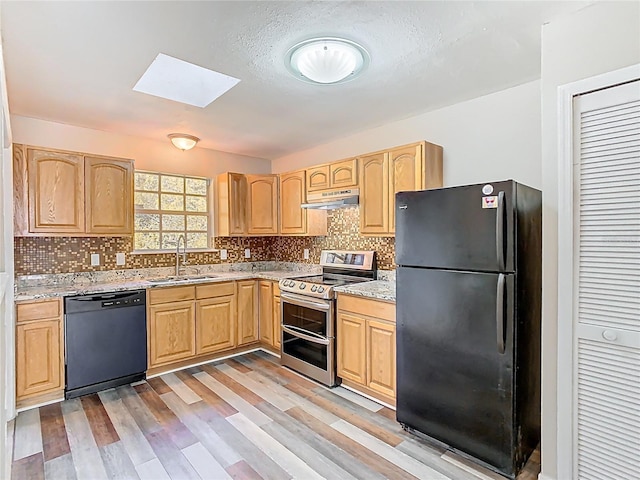 kitchen with light brown cabinets, under cabinet range hood, a skylight, black appliances, and a sink