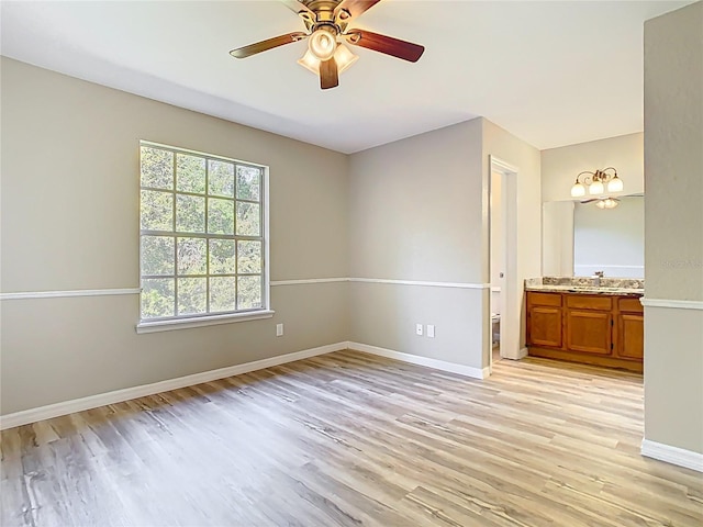 unfurnished bedroom featuring ensuite bathroom, a sink, light wood finished floors, baseboards, and ceiling fan