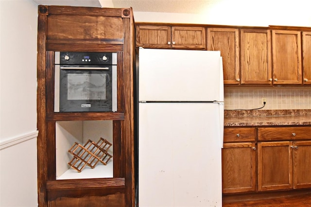 954 Courtyard Ln Unit 11, Orlando, FL 32825 - kitchen featuring decorative backsplash, brown cabinetry, double wall oven, dark countertops, and freestanding refrigerator