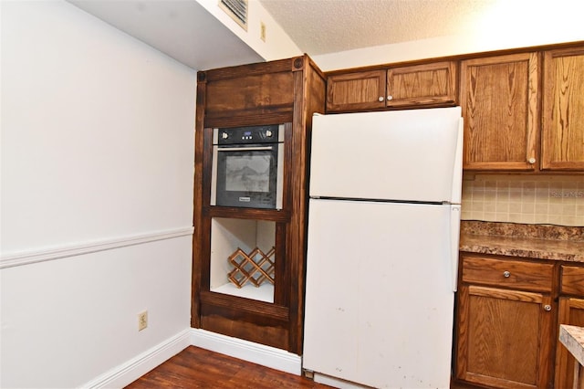 kitchen featuring oven, tasteful backsplash, dark hardwood / wood-style flooring, a textured ceiling, and white fridge