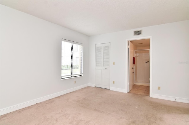 unfurnished bedroom with light carpet, a closet, and ensuite bath