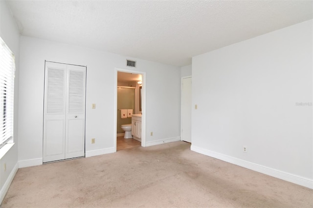 unfurnished bedroom featuring a closet, light carpet, a textured ceiling, and ensuite bathroom