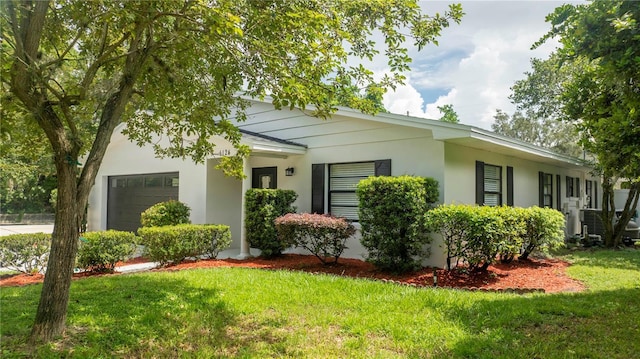ranch-style home featuring stucco siding, an attached garage, a front lawn, and driveway