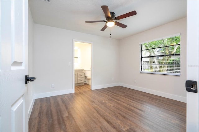 unfurnished bedroom featuring baseboards, wood finished floors, ceiling fan, and ensuite bath