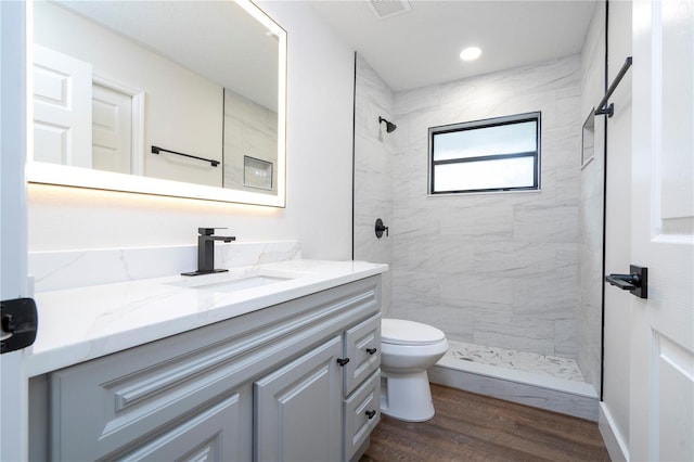 bathroom with toilet, tiled shower, vanity, wood finished floors, and visible vents