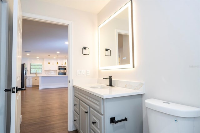 half bathroom with toilet, recessed lighting, wood finished floors, and vanity