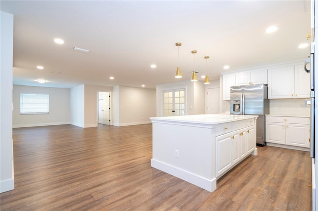 kitchen featuring white cabinets, light countertops, stainless steel fridge, wood finished floors, and a center island