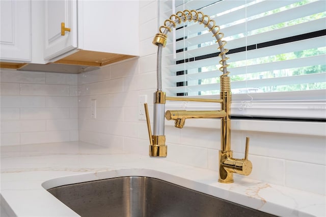 room details featuring light stone counters, sink, and white cabinets