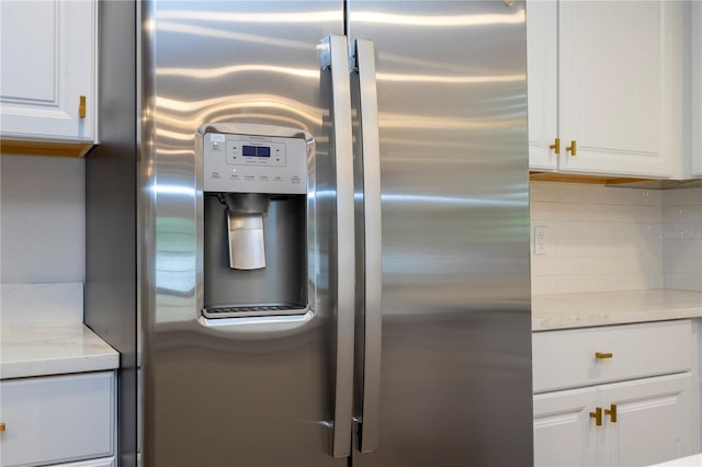 room details with light stone countertops, backsplash, stainless steel fridge with ice dispenser, and white cabinetry