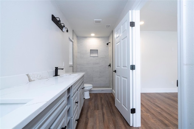 bathroom with vanity, toilet, a tile shower, and hardwood / wood-style flooring