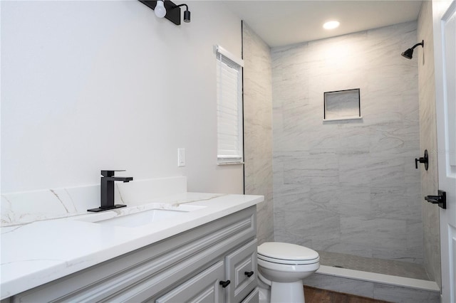 bathroom with toilet, a tile shower, hardwood / wood-style flooring, and vanity