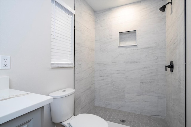 bathroom featuring toilet, a tile shower, and vanity