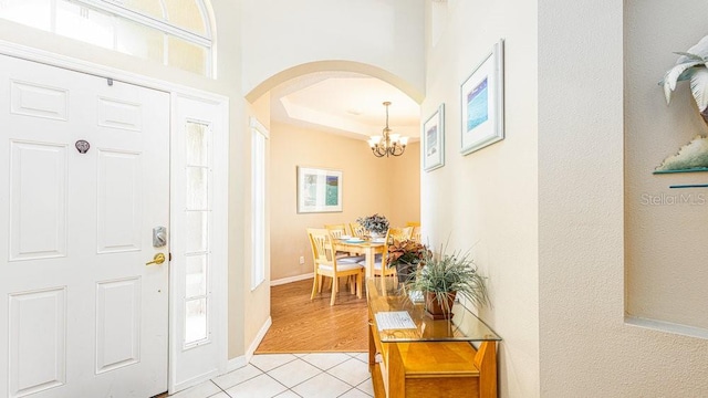 foyer with a raised ceiling, an inviting chandelier, and light tile patterned flooring