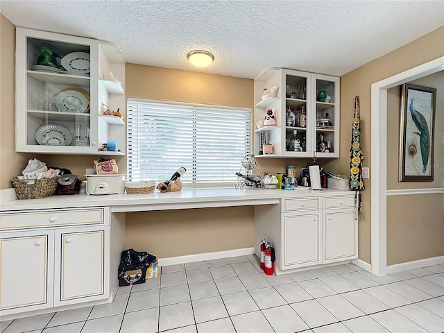 kitchen featuring built in desk, light tile patterned floors, white cabinets, and a textured ceiling