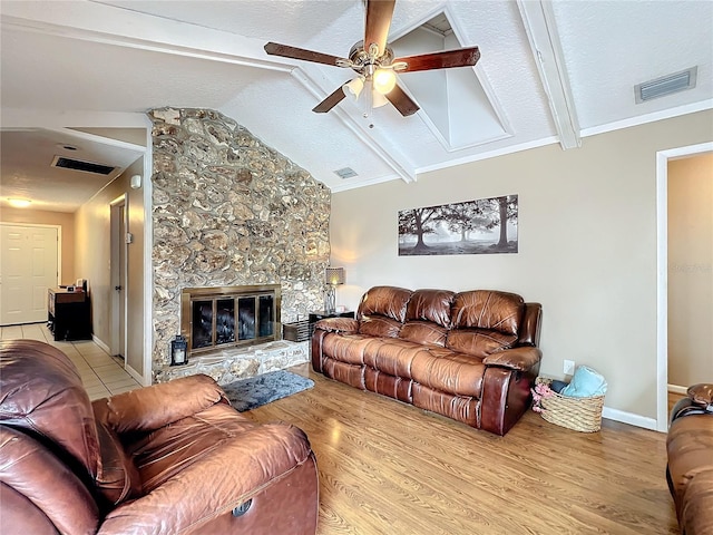 living room featuring a textured ceiling, light hardwood / wood-style flooring, a stone fireplace, ceiling fan, and vaulted ceiling with beams