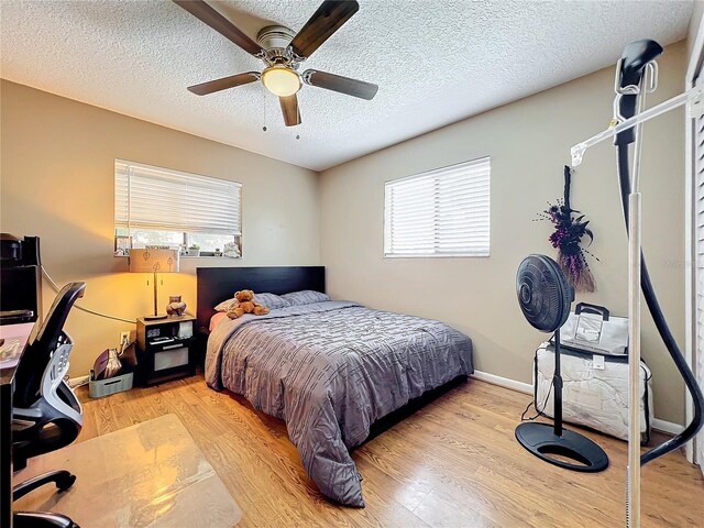 bedroom featuring light wood-type flooring, multiple windows, a textured ceiling, and ceiling fan