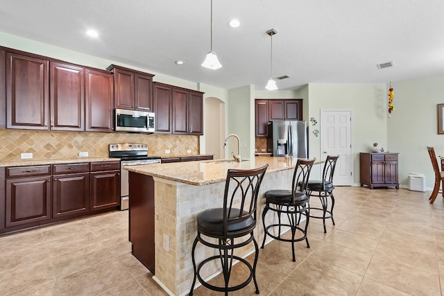 kitchen with a breakfast bar, sink, hanging light fixtures, a kitchen island with sink, and appliances with stainless steel finishes