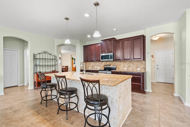 kitchen with decorative light fixtures, stainless steel appliances, tasteful backsplash, a kitchen breakfast bar, and a kitchen island with sink