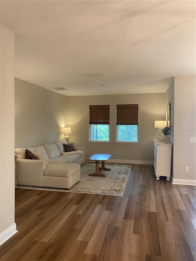 living room with dark wood-type flooring, a textured ceiling, baseboards, and visible vents