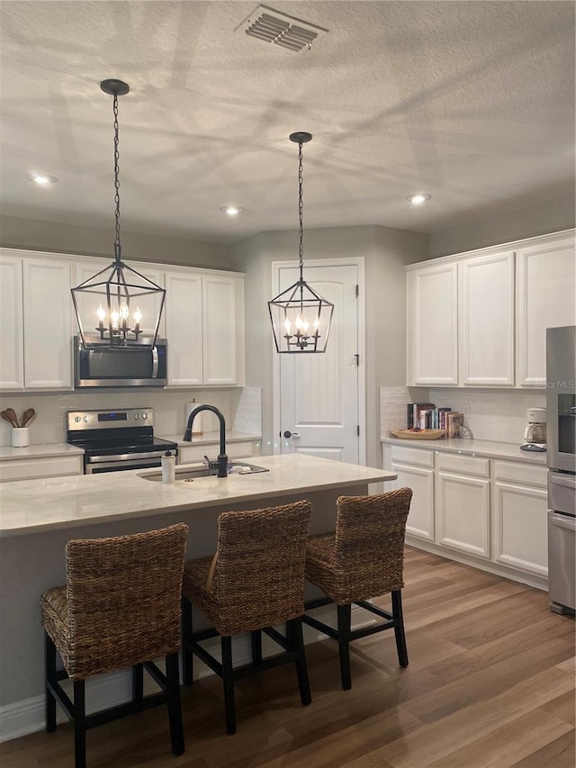 kitchen featuring appliances with stainless steel finishes, a chandelier, light hardwood / wood-style flooring, and white cabinets