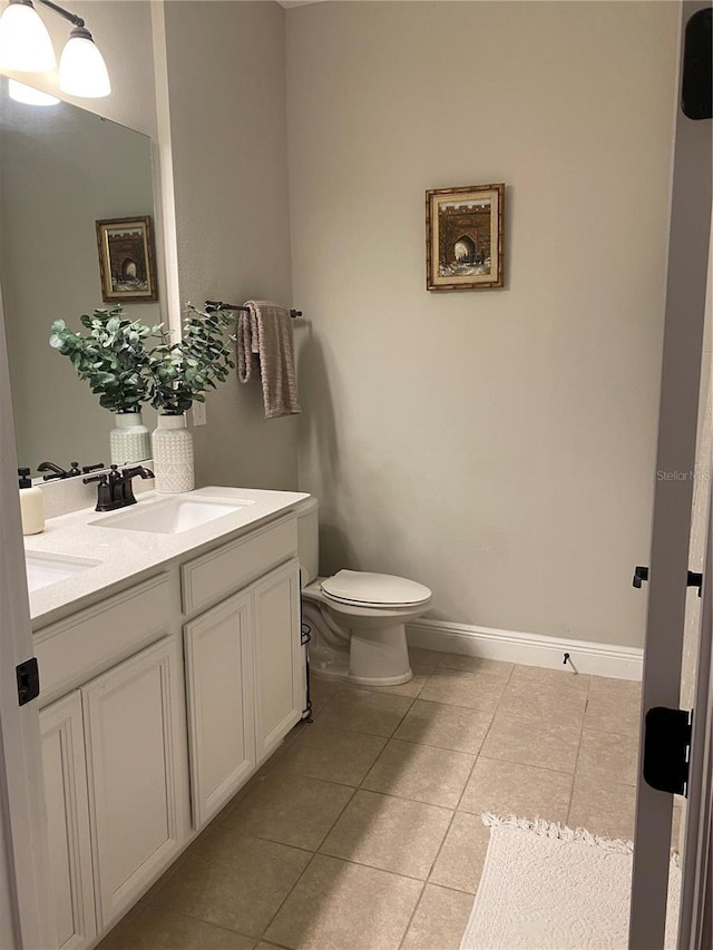 bathroom with tile patterned floors, a sink, double vanity, toilet, and baseboards