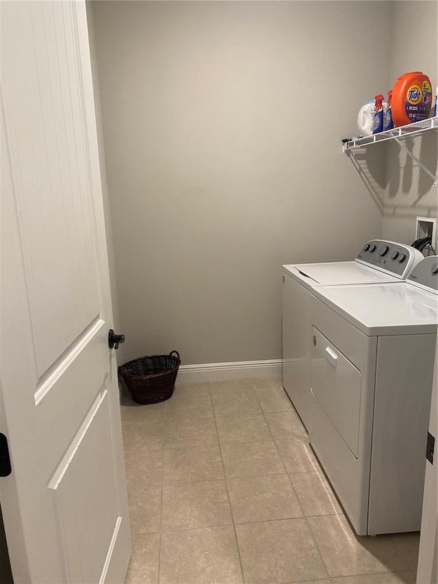 clothes washing area featuring baseboards, washer and clothes dryer, laundry area, and light tile patterned floors