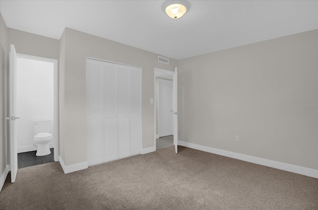 unfurnished bedroom featuring a closet, ensuite bathroom, and carpet