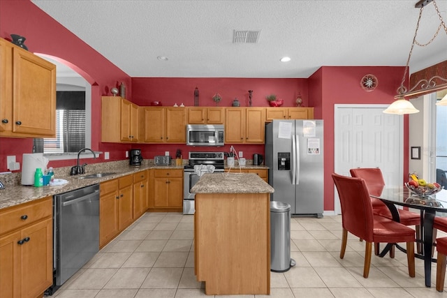 kitchen with a textured ceiling, a kitchen island, sink, light stone countertops, and appliances with stainless steel finishes