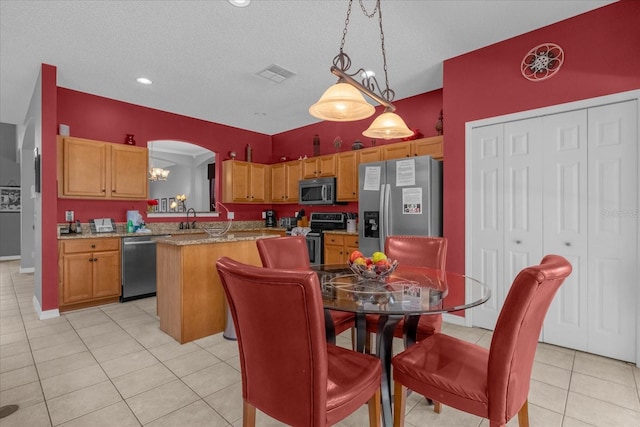 kitchen with a textured ceiling, light tile patterned floors, a kitchen island, sink, and appliances with stainless steel finishes