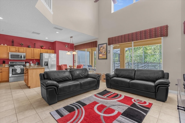 living room featuring a towering ceiling, a textured ceiling, light tile patterned floors, and ceiling fan