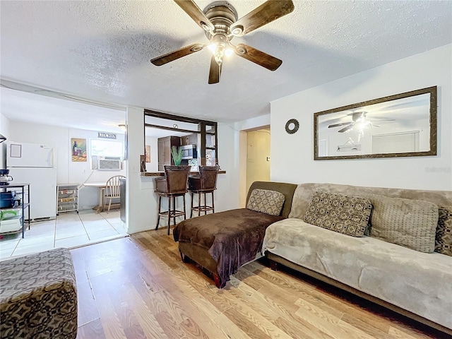 living room with ceiling fan, a textured ceiling, and light hardwood / wood-style flooring