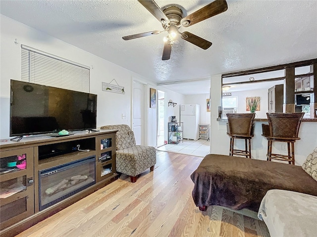 living room with light wood-type flooring, ceiling fan, and a textured ceiling