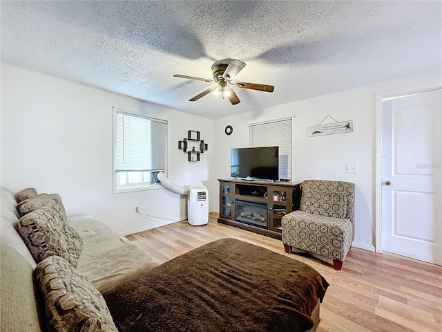 living room featuring light wood-type flooring, ceiling fan, and a textured ceiling