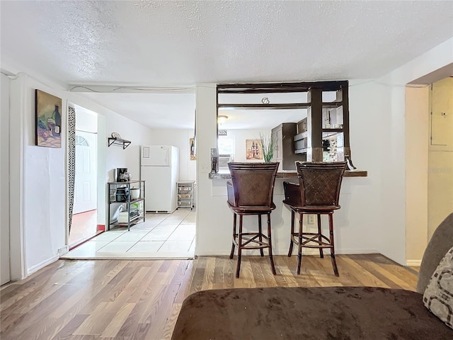 bar with light wood-type flooring, white refrigerator, and a textured ceiling