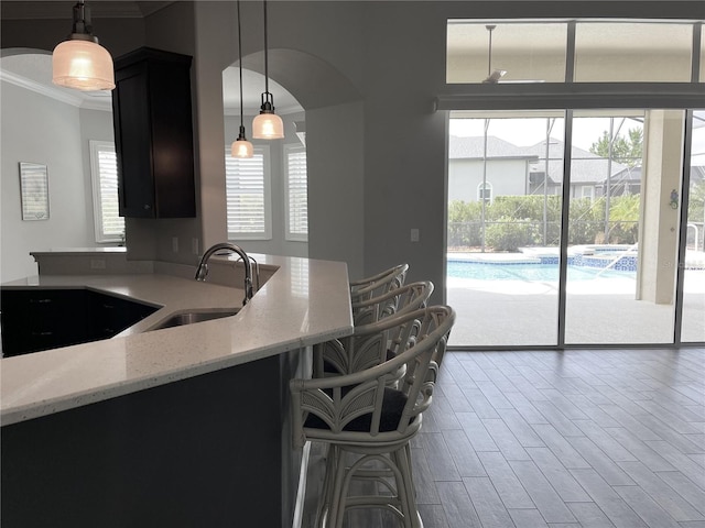 kitchen featuring crown molding, light stone countertops, sink, and pendant lighting