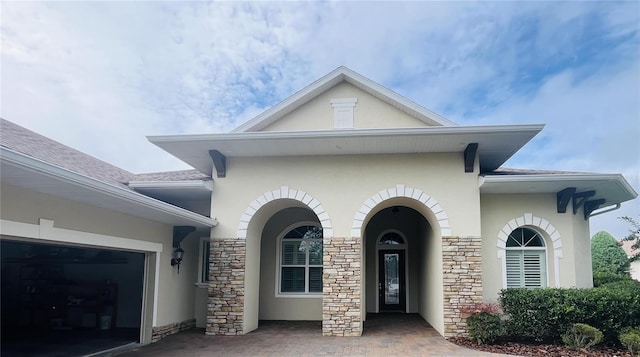 view of front of property featuring stucco siding, stone siding, driveway, and an attached garage