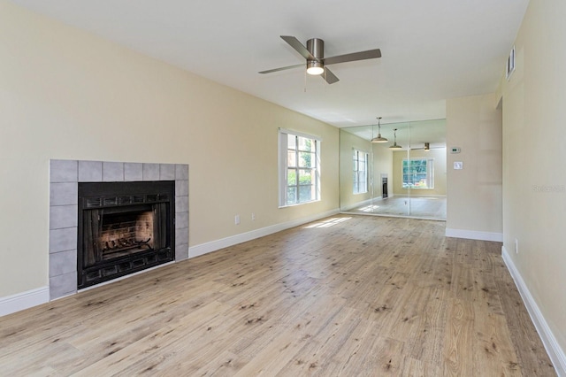 unfurnished living room with light wood-type flooring, ceiling fan, and a tiled fireplace