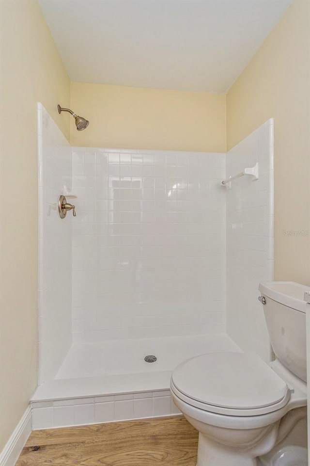 bathroom with tiled shower, wood-type flooring, and toilet