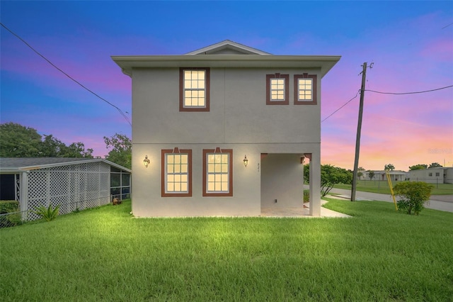 back house at dusk featuring a lawn