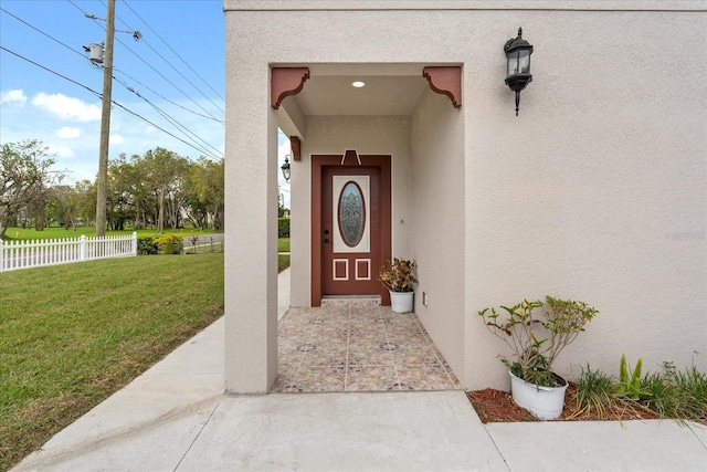 view of exterior entry featuring a lawn, fence, and stucco siding