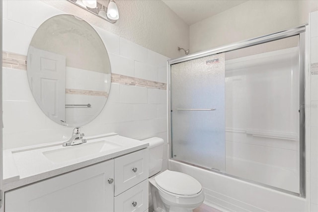 full bathroom featuring a textured wall, toilet, vanity, tile walls, and combined bath / shower with glass door